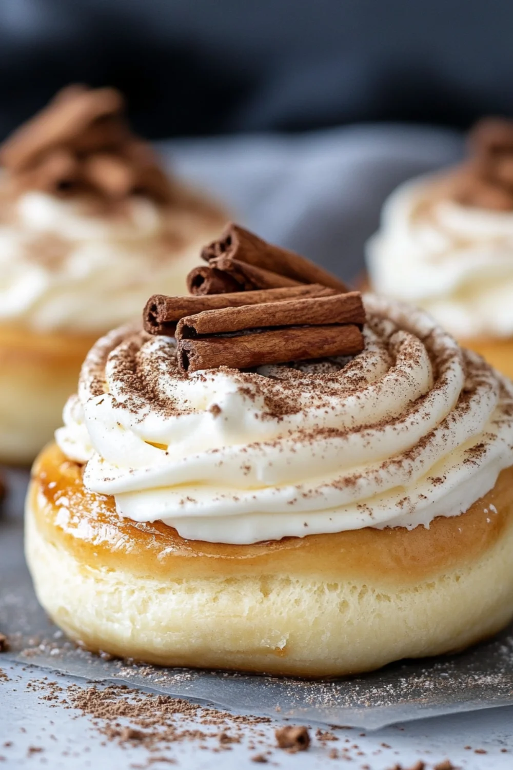 Close-up shot of freshly baked cinnamon buns with a swirl of cinnamon filling, topped with a glossy, smooth white frosting.