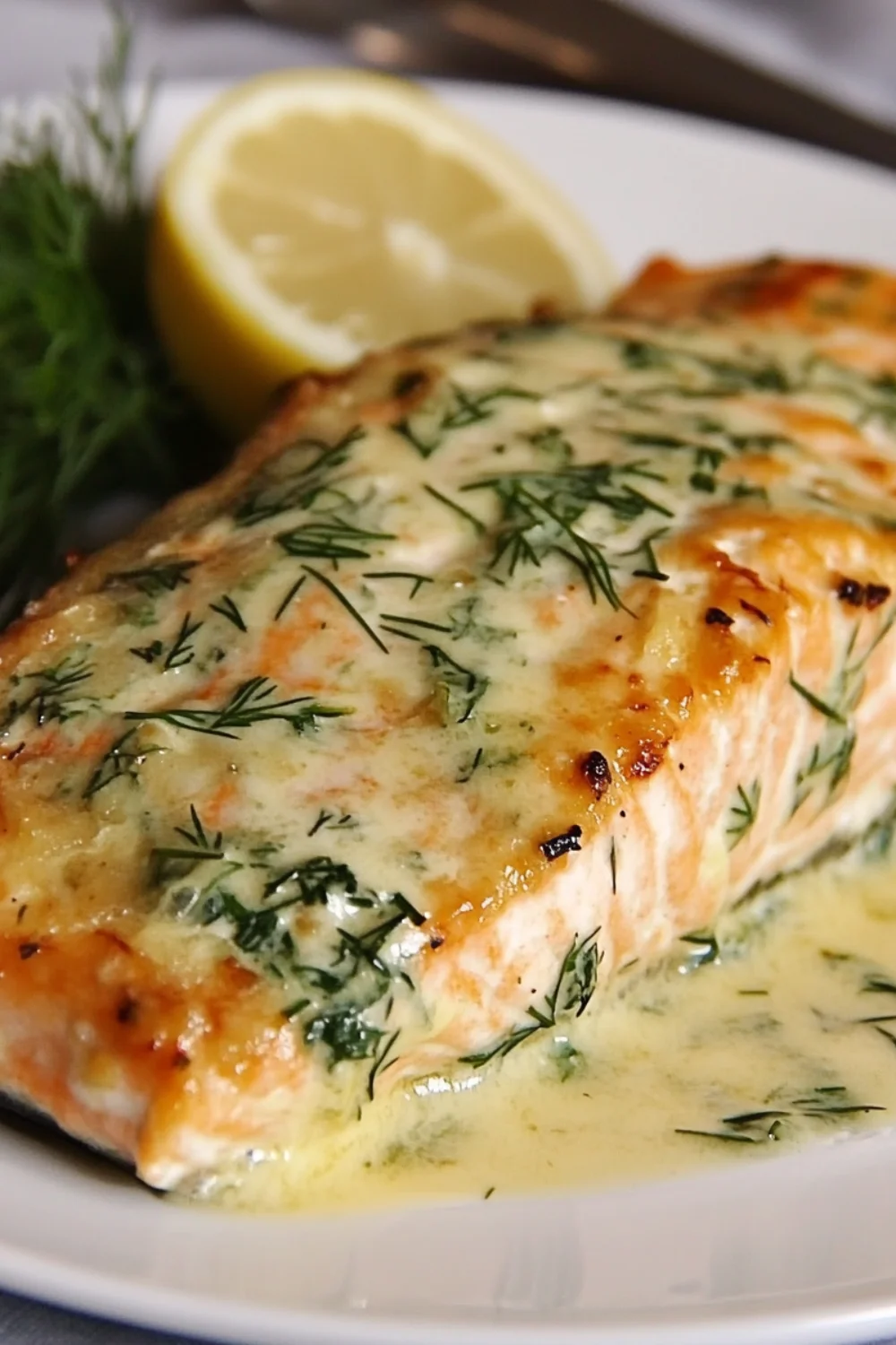 Baked salmon fillet topped with lemon slices and garnished with fresh dill, served on a bed of yellow vegetables and herbs.