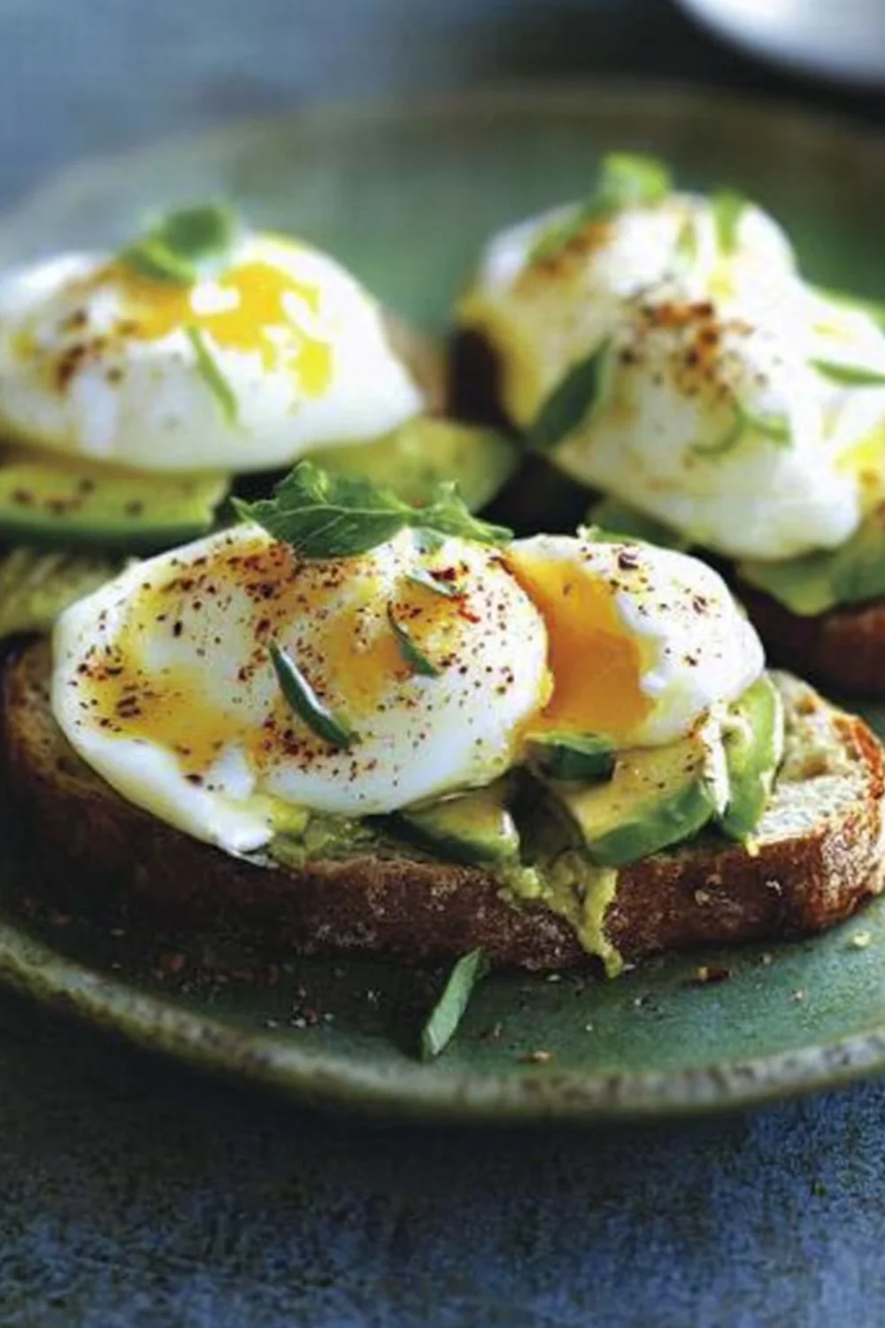 A delicious plate of avocado toast with poached eggs, topped with herbs and seasoning. The eggs are perfectly cooked with runny yolks, resting on a slice of toasted bread.