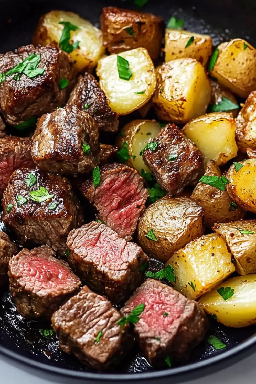 Juicy garlic butter steak bites and golden roasted potato cubes served in a skillet, garnished with fresh parsley.