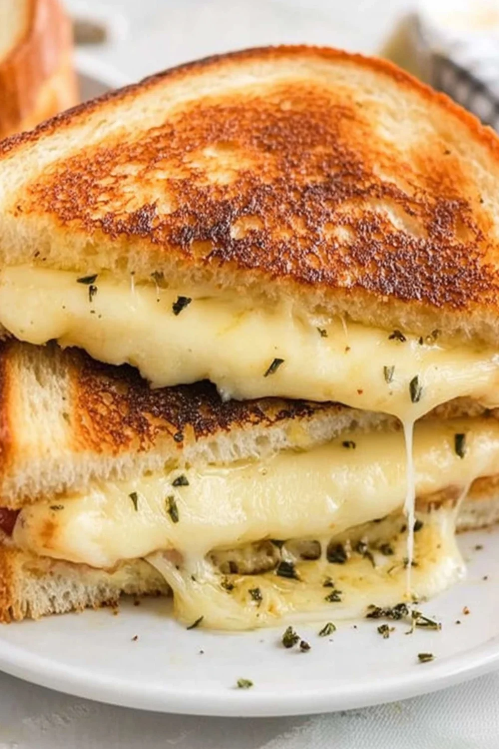 Close-up of a provolone grilled cheese sandwich, showing golden, crispy bread with melted provolone cheese stretching between the slices and sprinkled with herbs.