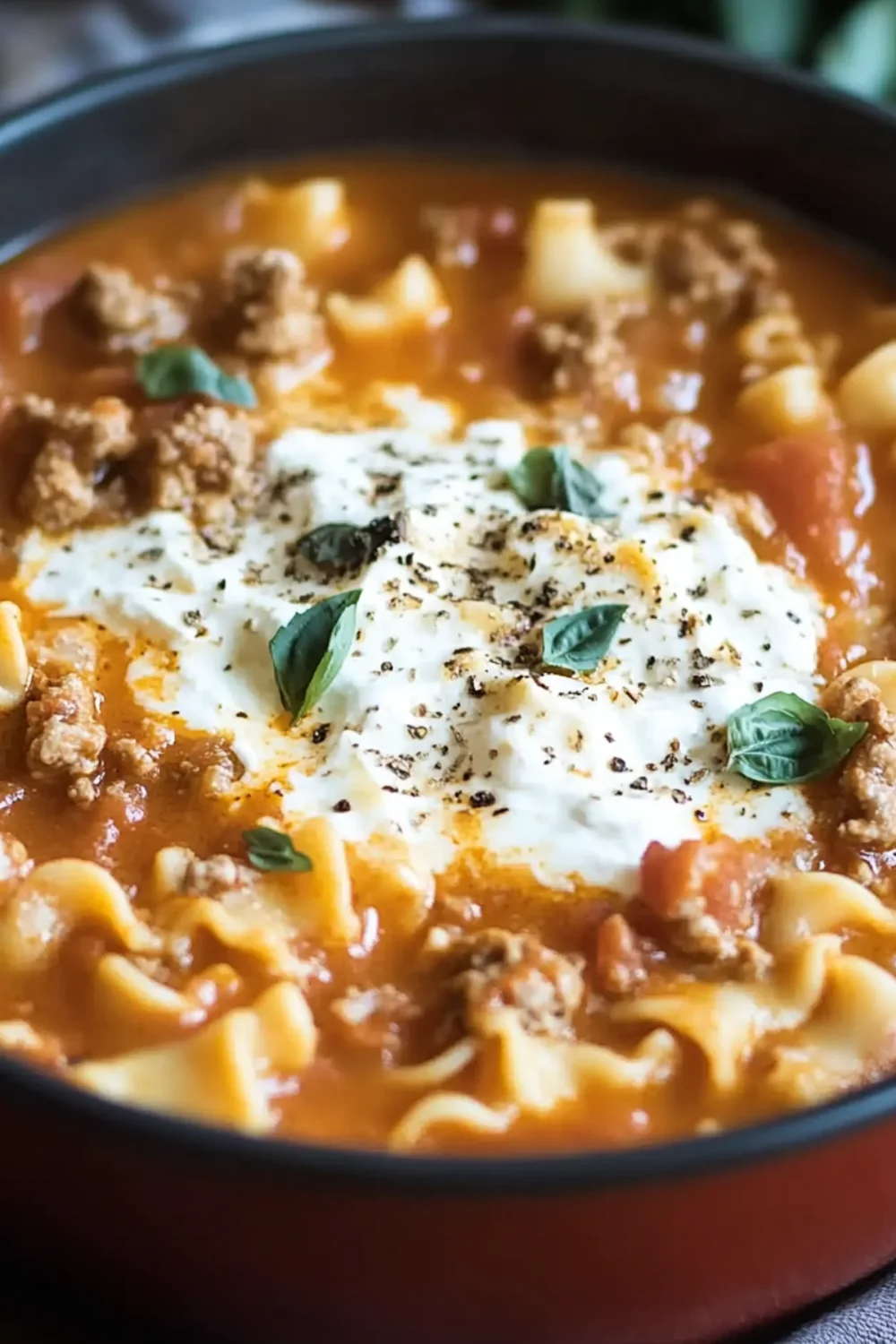 Close-up of one pot lasagna soup with ground meat, lasagna noodles, tomato broth, ricotta, and fresh basil garnish in a black pot.