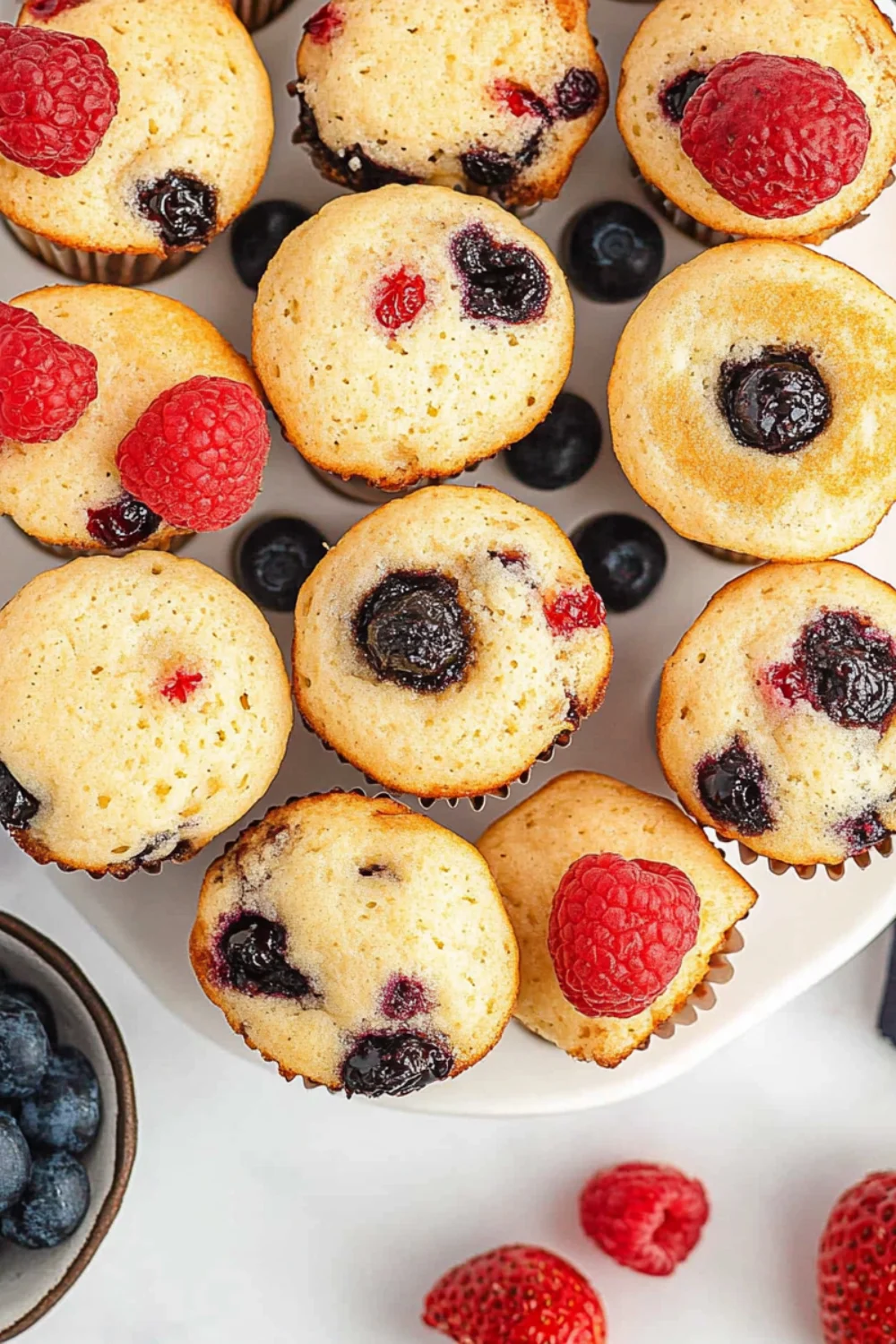 Close-up view of fluffy pancake mini muffins topped with fresh raspberries and blueberries, showcasing their soft texture and fruit-filled interior.