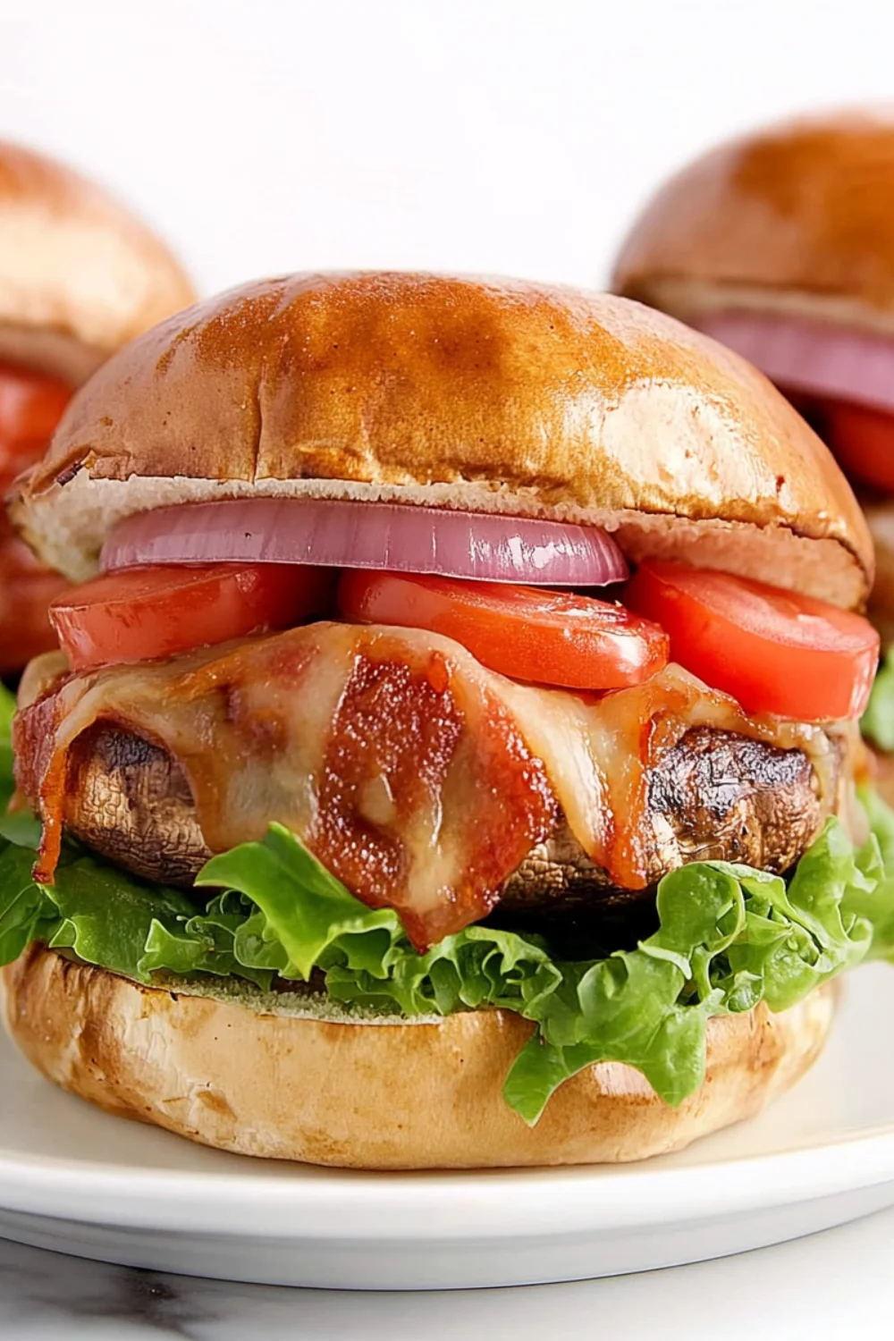 Close-up of a gourmet peanut butter bacon burger with melted cheese, tomato slices, red onion, and lettuce on a toasted brioche bun.