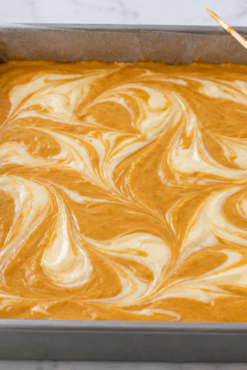 Unbaked pumpkin and ivory cheesecake batter gently marbled in a parchment-lined square pan